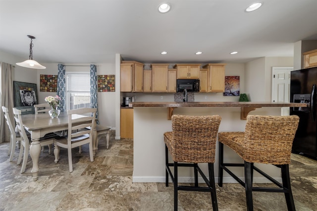 kitchen with black appliances, light brown cabinets, a breakfast bar area, and recessed lighting