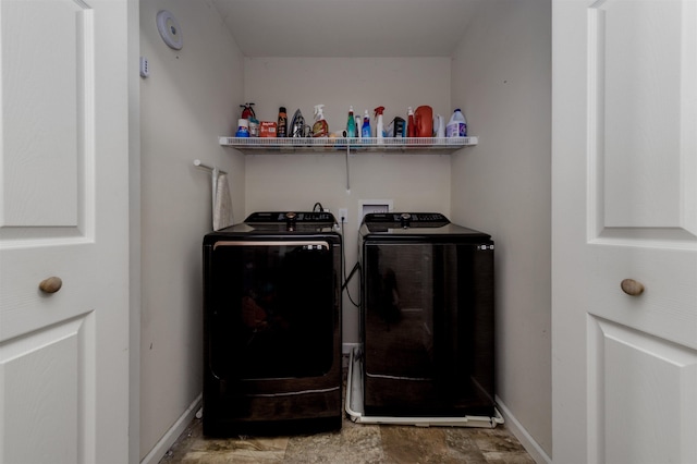 washroom featuring laundry area, baseboards, stone finish flooring, and washing machine and clothes dryer