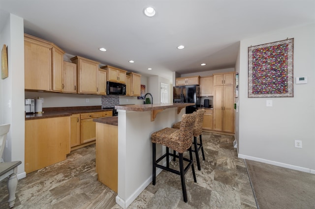 kitchen with baseboards, a breakfast bar area, light brown cabinetry, black appliances, and recessed lighting