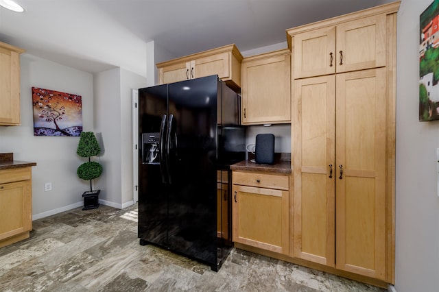 kitchen with dark countertops, black refrigerator with ice dispenser, baseboards, and light brown cabinetry