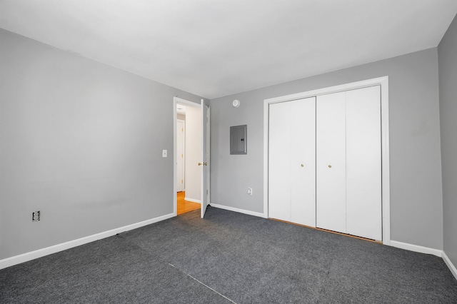 unfurnished bedroom with a closet, electric panel, dark carpet, and baseboards