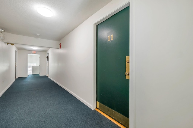 hall featuring baseboards, dark carpet, and a textured ceiling