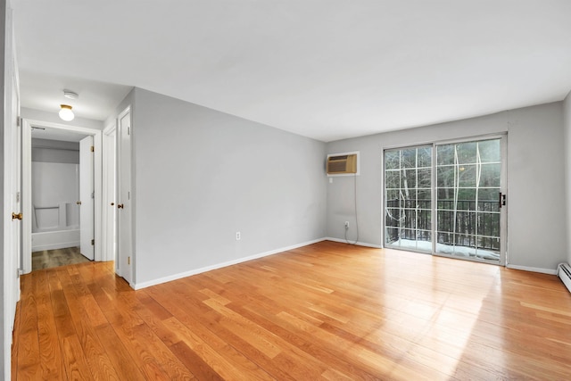 empty room featuring light wood-style floors, a wall mounted air conditioner, and baseboards