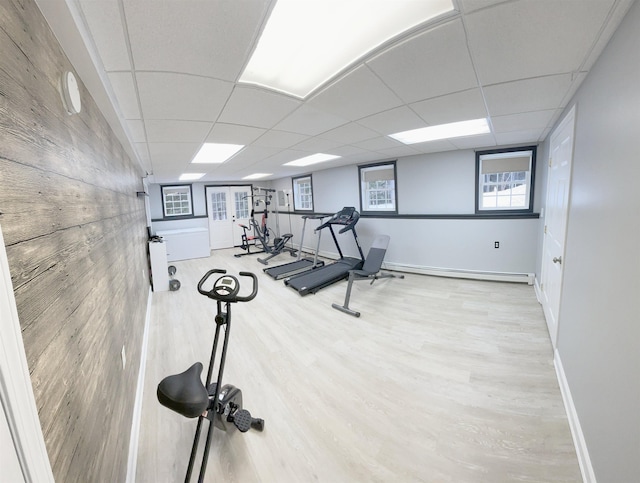 exercise room featuring a drop ceiling, baseboards, baseboard heating, and wood finished floors