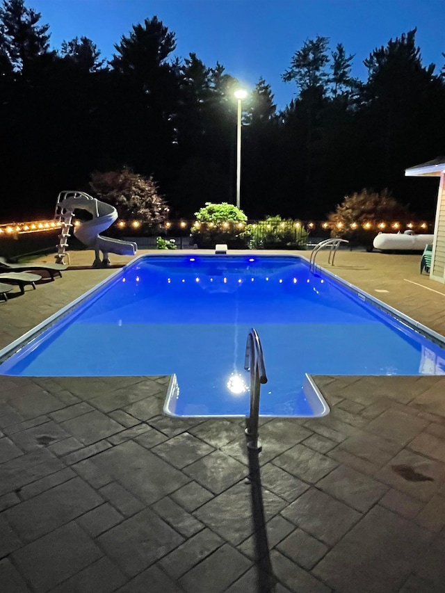 pool at twilight featuring an outdoor pool, a water slide, and a patio