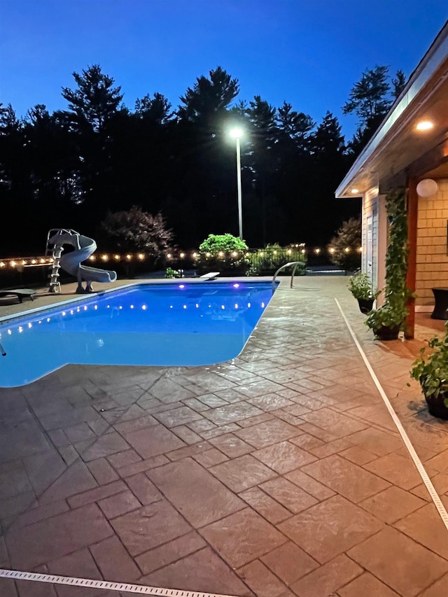 pool at night with an outdoor pool, a water slide, and a patio