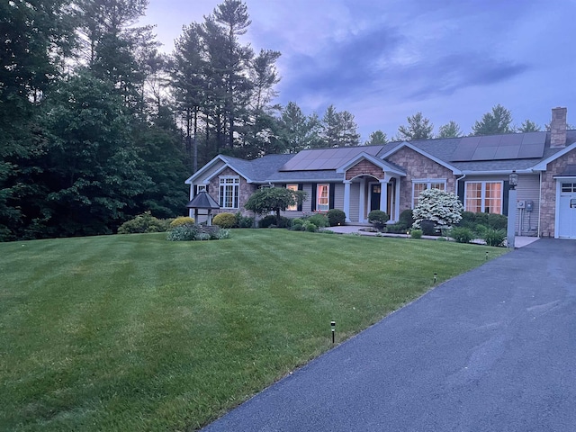 view of front of house with a front yard, stone siding, and roof mounted solar panels