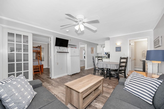 living area with ornamental molding, a ceiling fan, baseboards, and wood finished floors