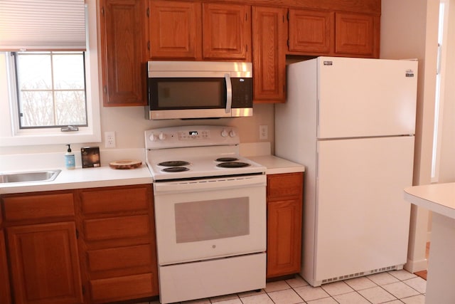 kitchen with white appliances, light tile patterned floors, brown cabinetry, light countertops, and a sink