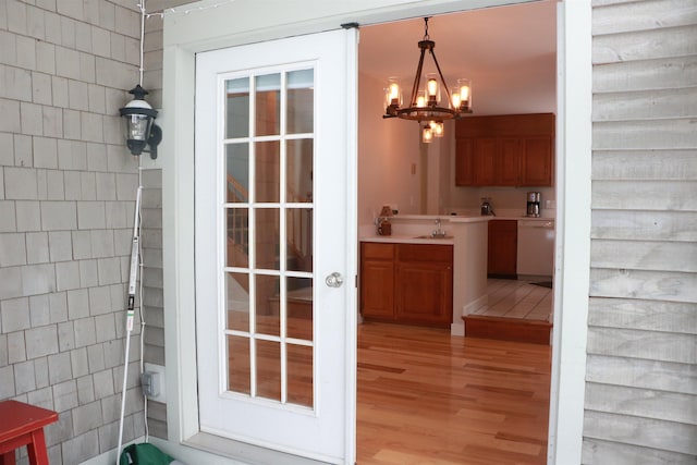 interior space with light wood-style flooring, a notable chandelier, a sink, and tile walls