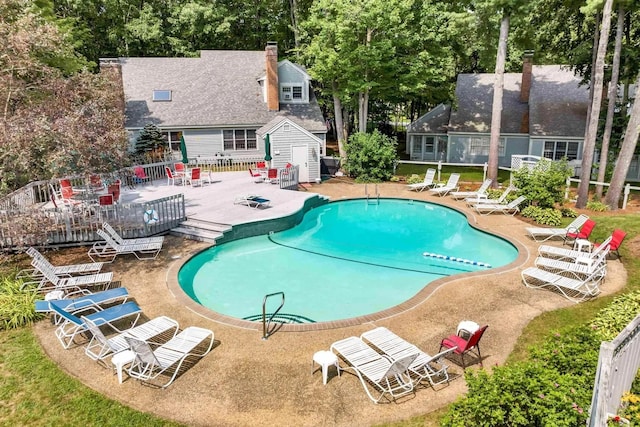 pool with a patio area, fence, and an outbuilding