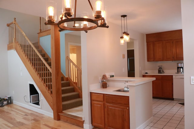 kitchen with a sink, light countertops, dishwasher, brown cabinetry, and decorative light fixtures