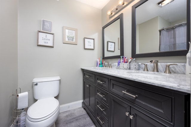 bathroom with baseboards, a sink, toilet, and double vanity