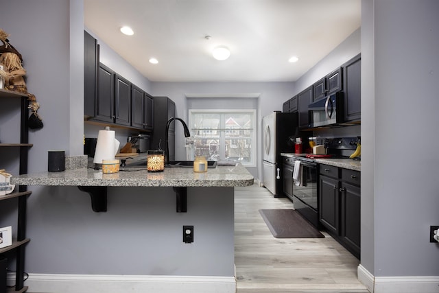 kitchen with electric range, stainless steel microwave, a breakfast bar, light stone counters, and a peninsula