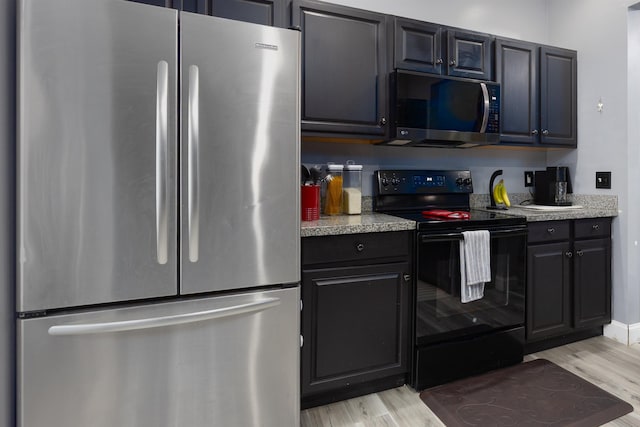 kitchen with black electric range, light wood-type flooring, light countertops, and freestanding refrigerator