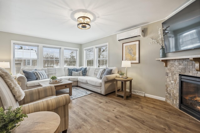 living area with a stone fireplace, wood finished floors, visible vents, a healthy amount of sunlight, and a wall mounted air conditioner