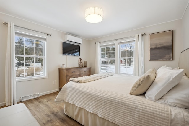 bedroom featuring light wood-style floors, baseboards, visible vents, and a wall mounted AC