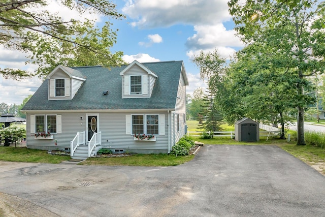 cape cod-style house featuring roof with shingles, an outdoor structure, driveway, and a storage unit