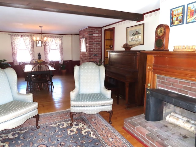 sitting room with a brick fireplace, beamed ceiling, an inviting chandelier, and wood finished floors