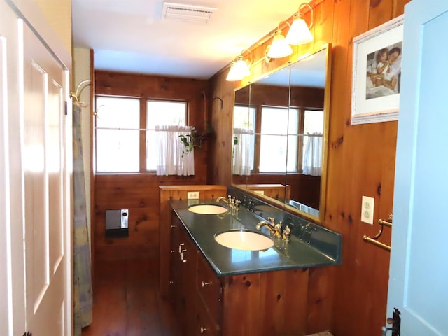 bathroom with double vanity, wood walls, a sink, and visible vents