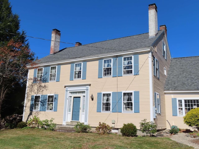 colonial house featuring a chimney and a front yard