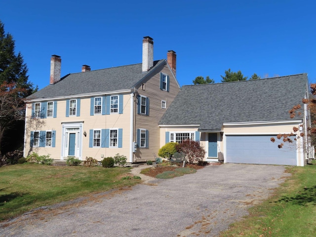 colonial-style house featuring a front lawn, a chimney, an attached garage, and aphalt driveway