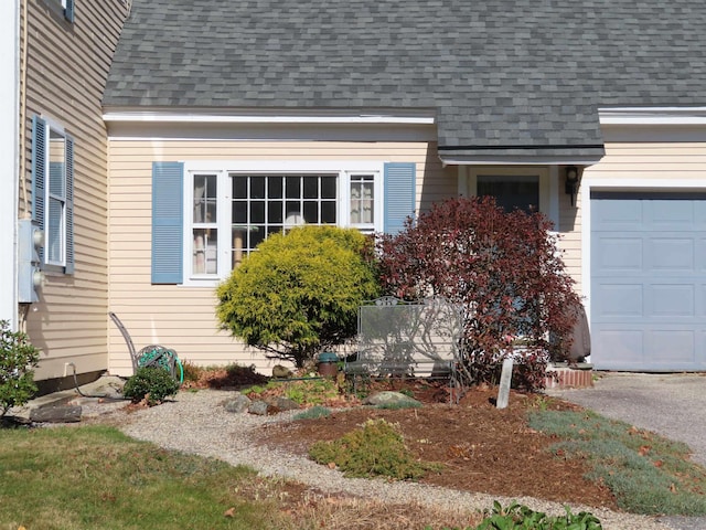 view of exterior entry featuring an attached garage and roof with shingles