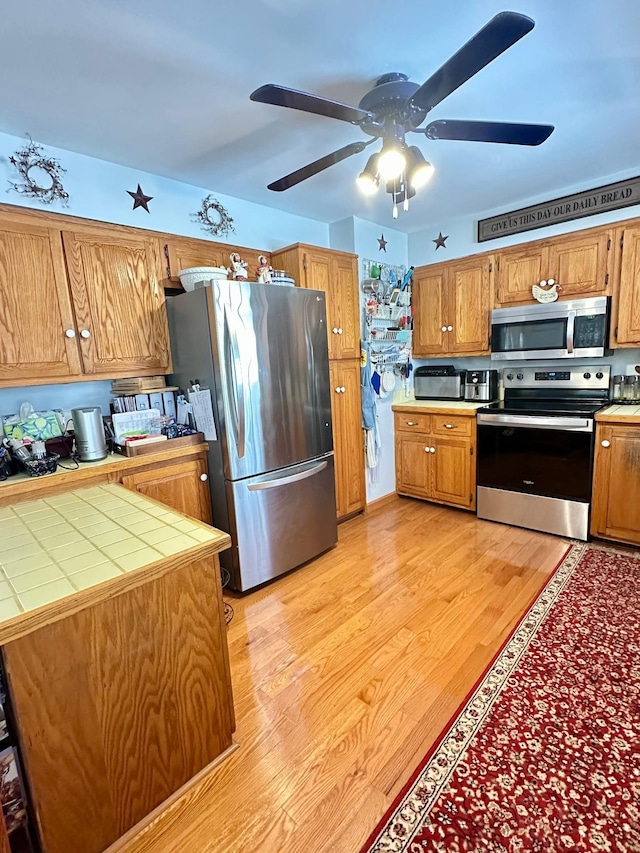 kitchen featuring tile countertops, light wood-style flooring, brown cabinets, and stainless steel appliances