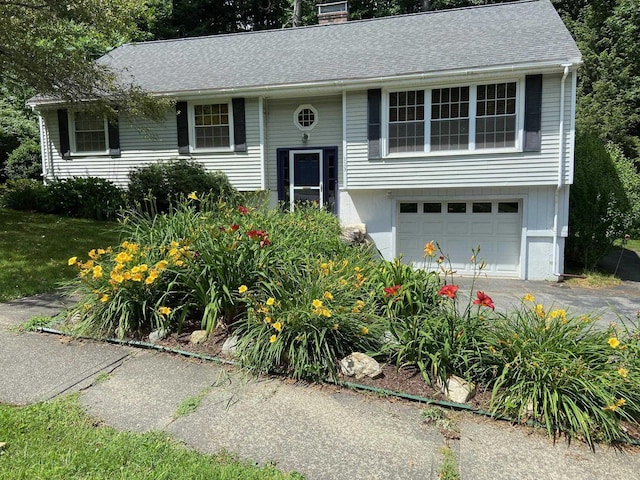 bi-level home with a shingled roof, driveway, a chimney, and an attached garage