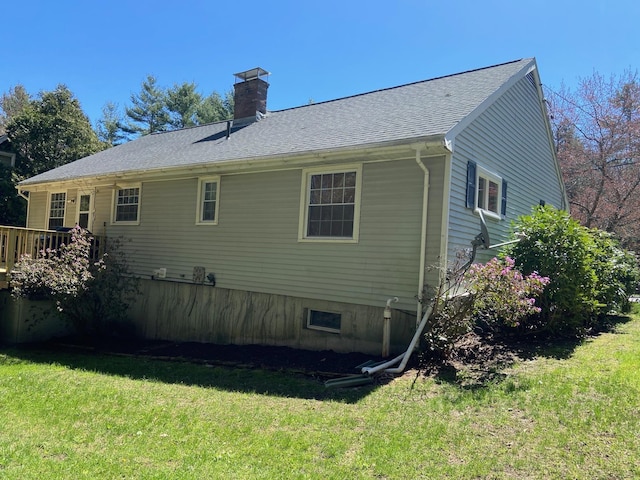 rear view of house featuring roof with shingles, a chimney, and a yard