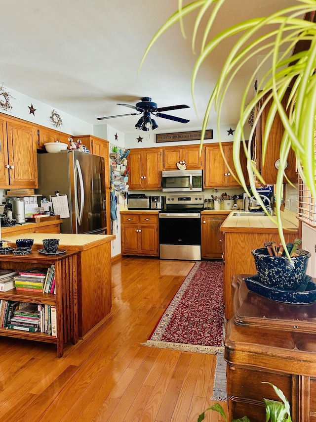 kitchen with tile countertops, light wood-style flooring, appliances with stainless steel finishes, brown cabinetry, and a sink