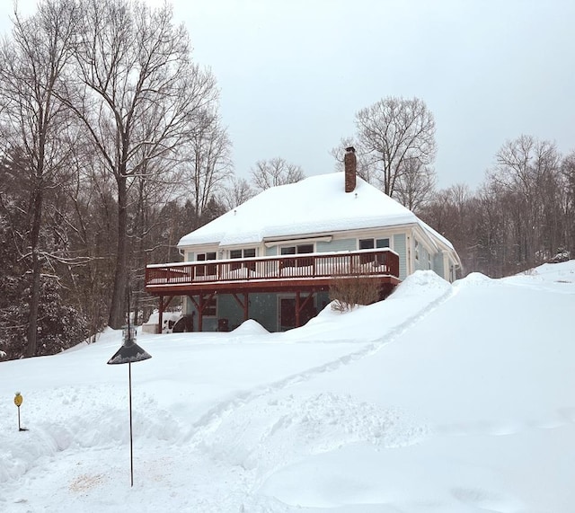 snow covered back of property with a garage, a chimney, and a wooden deck