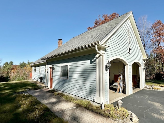 view of side of home with a garage, a chimney, a lawn, and roof with shingles