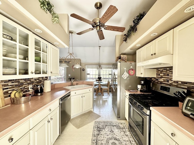 kitchen with under cabinet range hood, stainless steel appliances, a peninsula, a sink, and backsplash