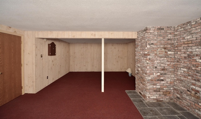 finished below grade area featuring wooden walls, dark colored carpet, electric panel, and a textured ceiling