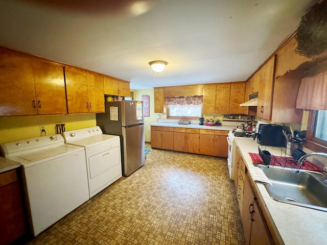 kitchen with white gas range oven, freestanding refrigerator, under cabinet range hood, separate washer and dryer, and a sink