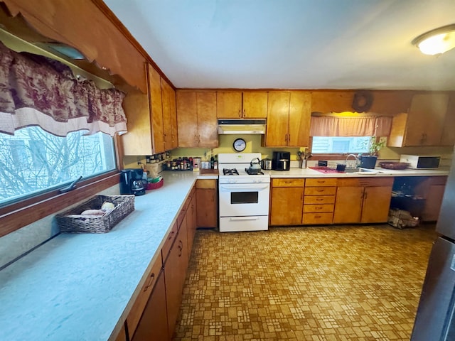 kitchen featuring brown cabinets, light countertops, white gas stove, under cabinet range hood, and a sink