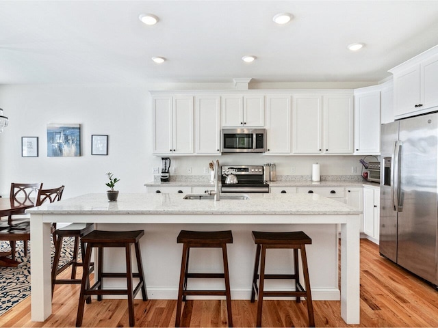 kitchen featuring light wood finished floors, appliances with stainless steel finishes, white cabinetry, a sink, and a kitchen bar