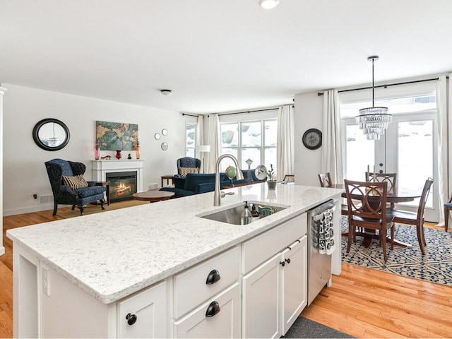 kitchen featuring dishwasher, light wood-style flooring, a sink, and a glass covered fireplace