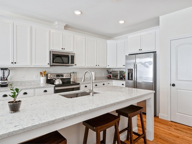 kitchen featuring appliances with stainless steel finishes, a kitchen bar, a sink, and white cabinets