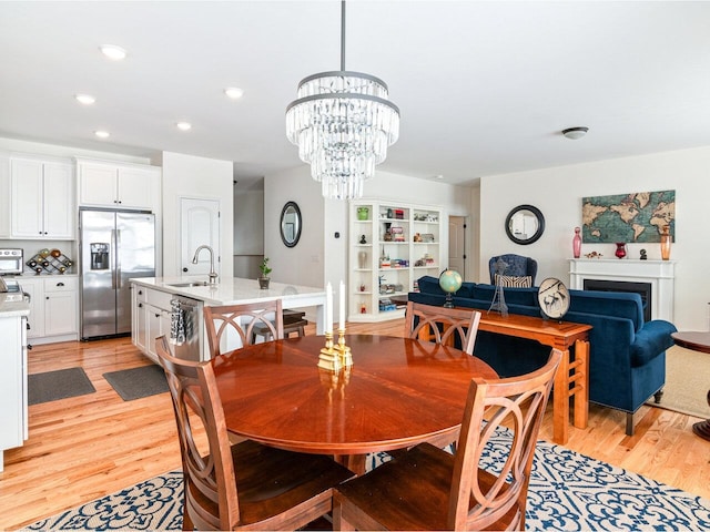 dining space featuring light wood finished floors, a fireplace, a chandelier, and recessed lighting