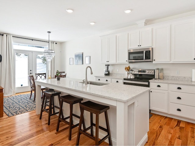 kitchen featuring light wood finished floors, a kitchen island with sink, stainless steel appliances, white cabinetry, and a sink