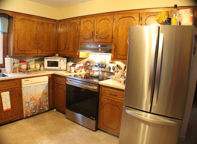 kitchen with appliances with stainless steel finishes, light countertops, brown cabinets, and under cabinet range hood