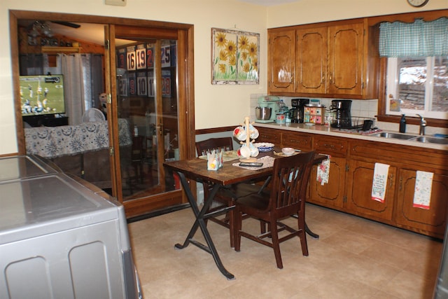 kitchen with brown cabinets, washing machine and clothes dryer, a sink, light countertops, and backsplash