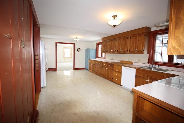 kitchen with white appliances, baseboards, brown cabinets, light floors, and a sink