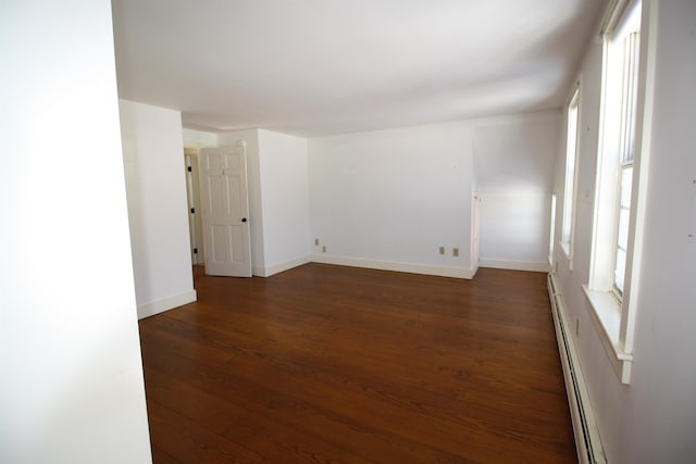 spare room with a baseboard heating unit, baseboards, and dark wood finished floors