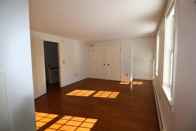 spare room featuring a baseboard heating unit, baseboards, and wood finished floors