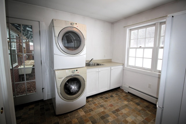 washroom featuring baseboard heating, a sink, cabinet space, and stacked washer / drying machine