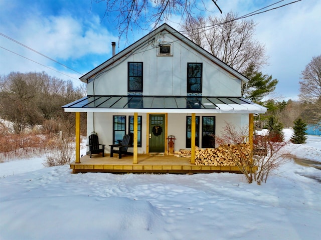 snow covered rear of property with metal roof, a porch, and a standing seam roof