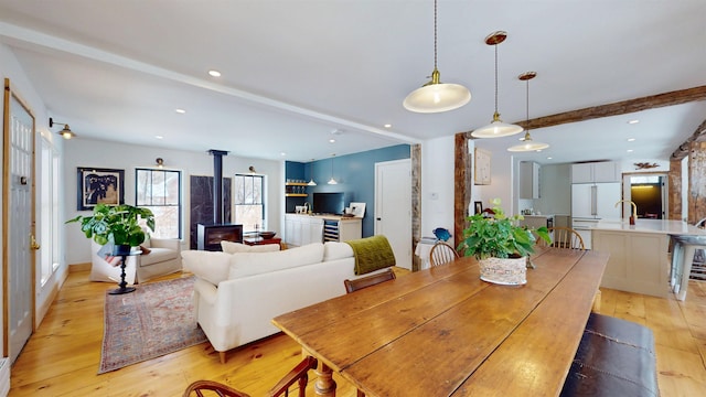 dining room featuring a wood stove, light wood-style flooring, beamed ceiling, and recessed lighting